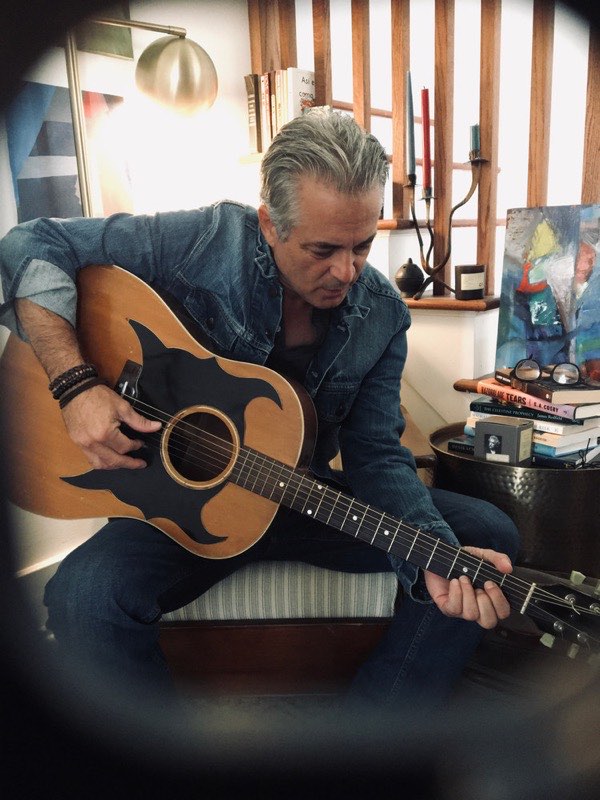 Stacy Dean Campbell playing an acoustic guitar at home.